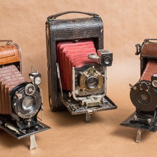 Three vintage folding cameras standing side by side