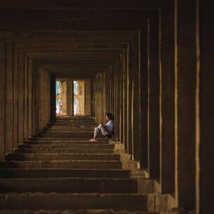 Person seated in a symmetrical stone corridor
