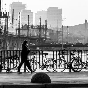 Pedestrian walking past a riverside bike rack, city skyline behind