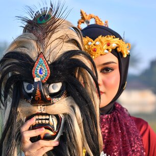 Traditional masked performer beside a woman in ceremonial dress