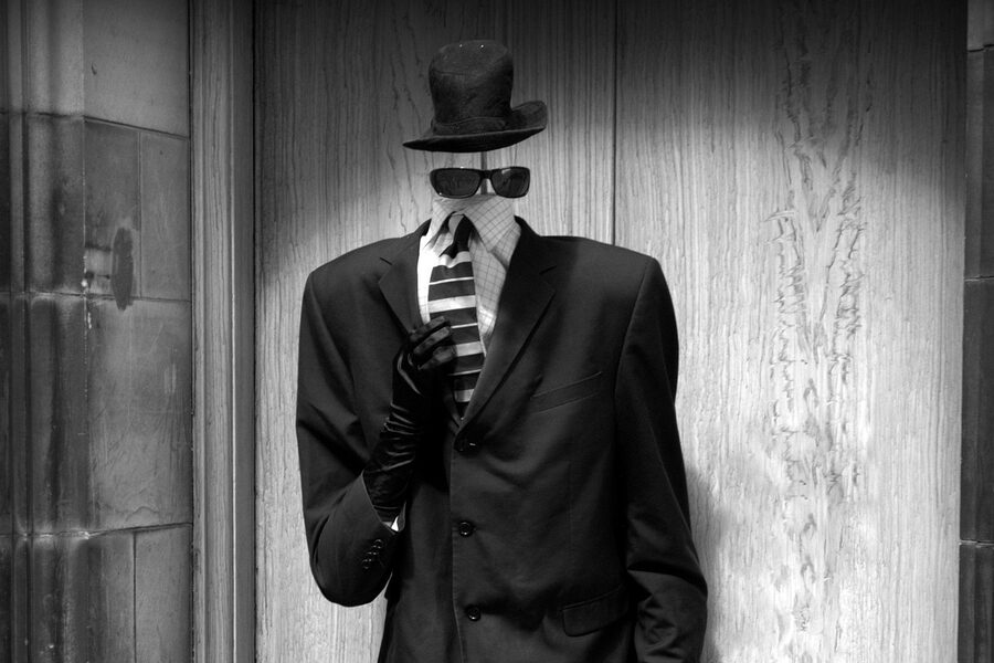 Black-and-white photo of a faceless mannequin in a suit, hat, and sunglasses