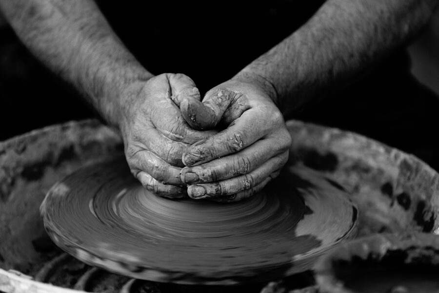 Black-and-white photo of a potter's hands shaping clay on a wheel