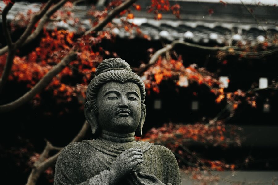 Stone Buddha statue framed by autumn maple leaves